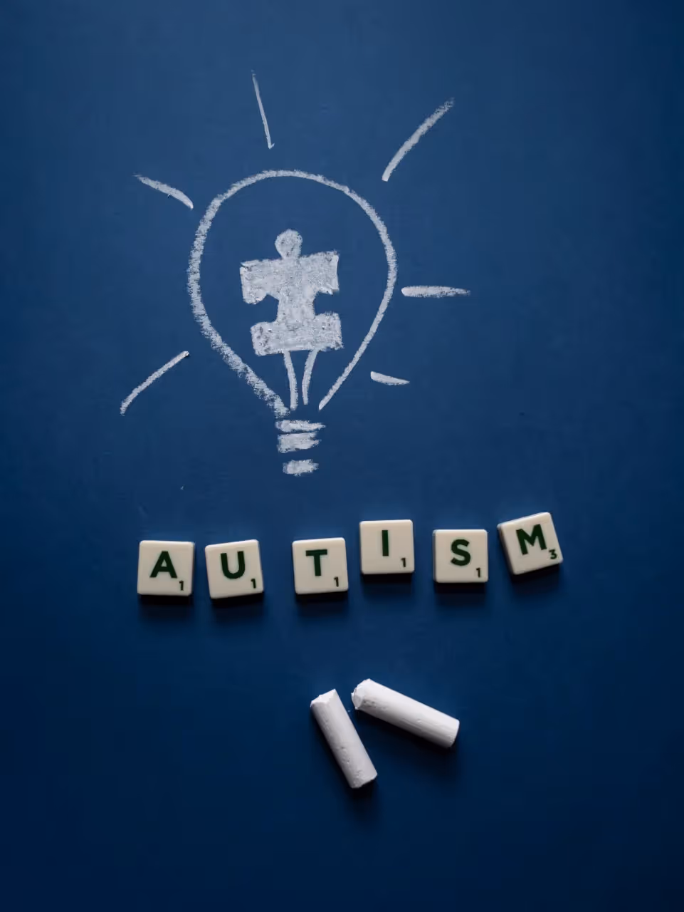 Autism puzzle piece drawn in chalk inside a chalk-drawn lightbulb with the word autism spelled out below with beads