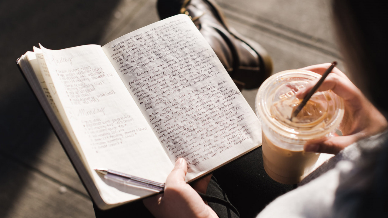 Person holding a journal open in one hand and a coffee in the other.