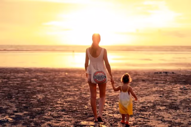 Woman and her young child walking on sand near water