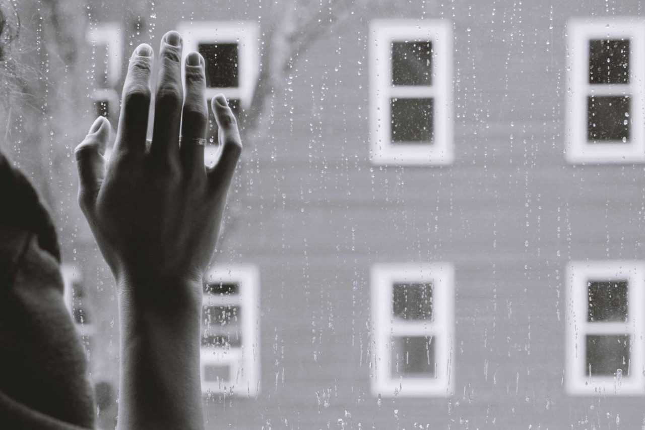 a person with their hand on a window as it rains outside