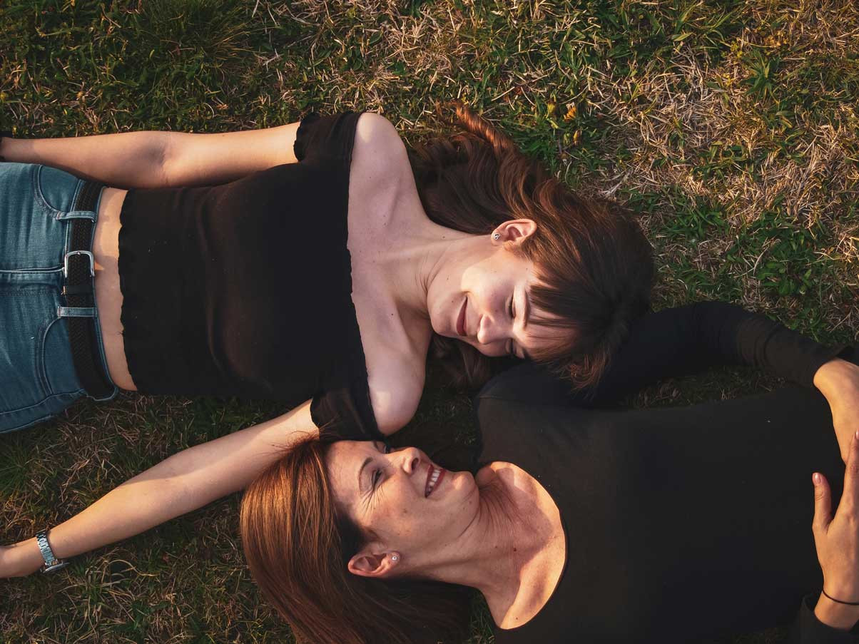 mother and daughter lying on grass looking at each other