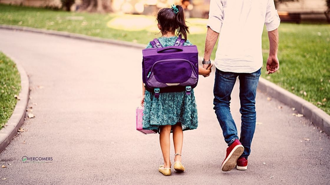 A girl walking with her dad holding his hand.