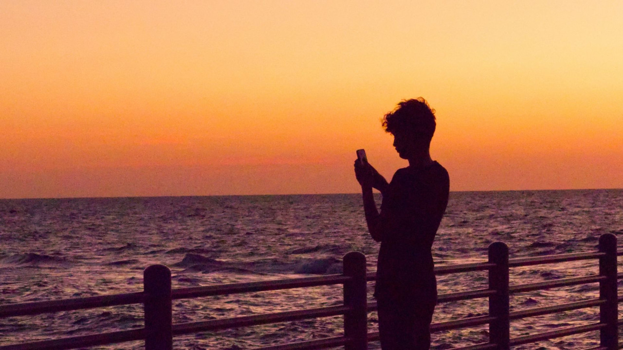 a young person looking at their phone next to the ocean