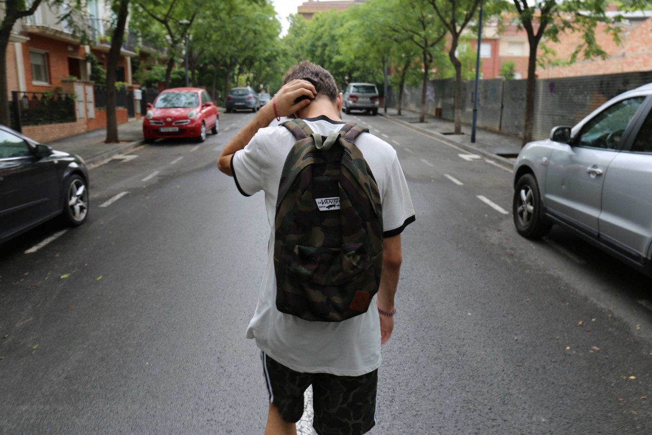 A person walking down the middle of the street wearing a backpack.