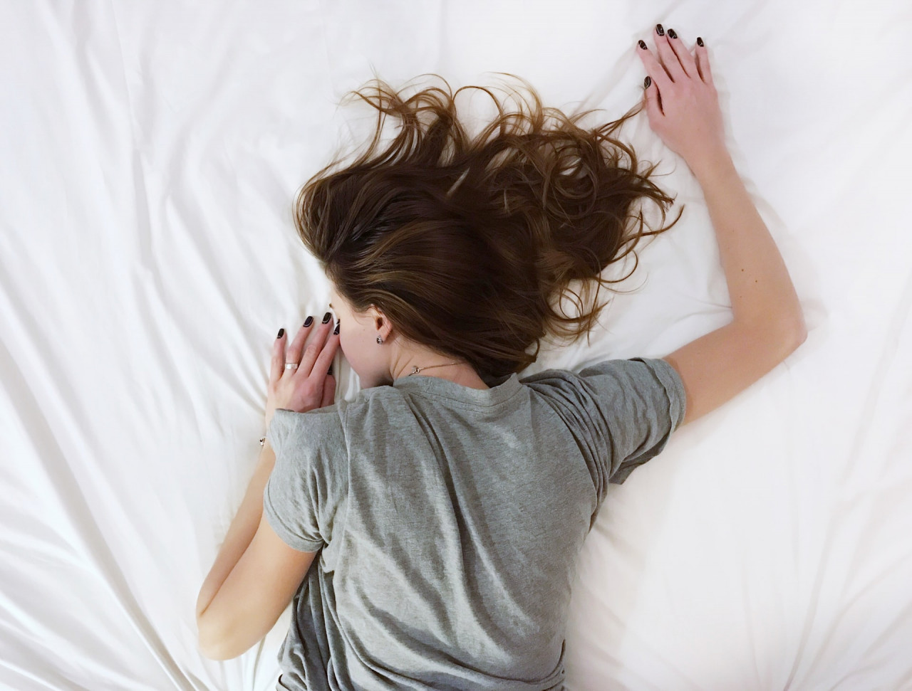 Exhausted woman laying on a bed with white sheets