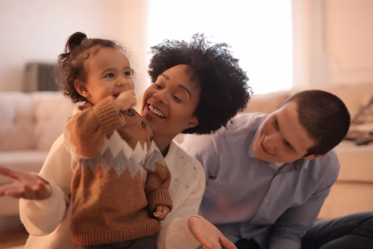 A mom and dad sitting on the floor with their smiling daughter