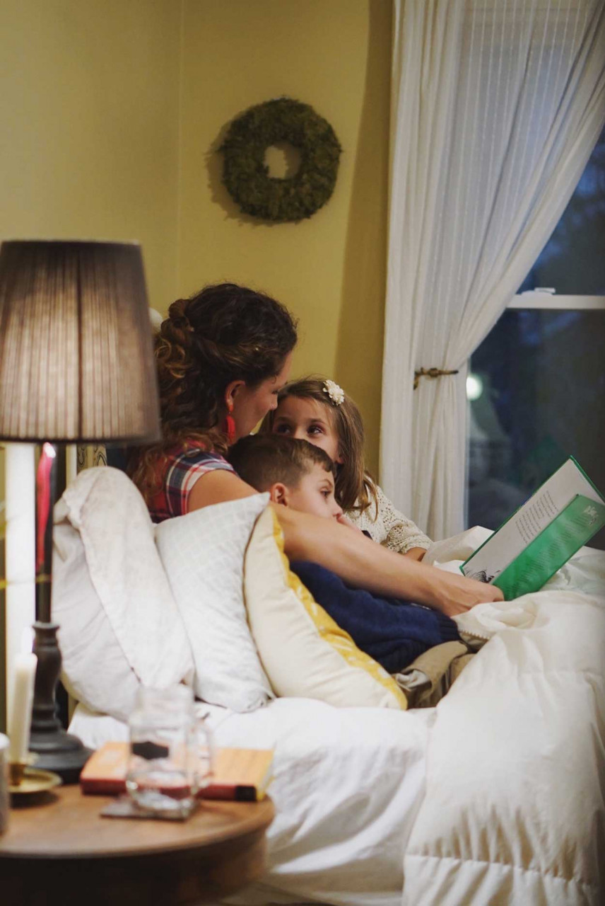 A mom and her two kids laying in bed reading a book