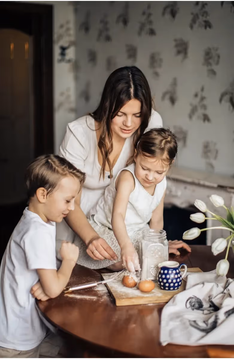 A mom and her 2 young children using flour and eggs
