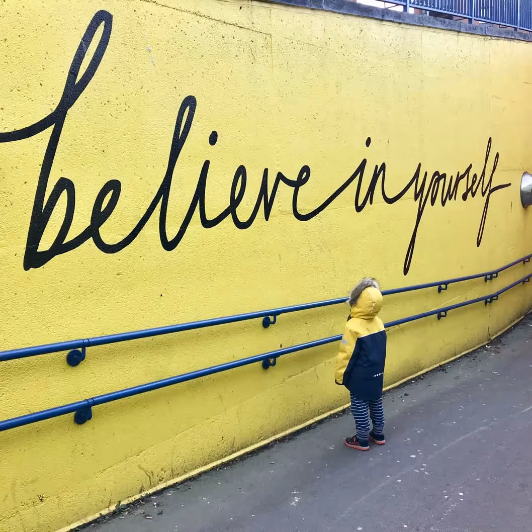 a child looking at words on a wall that say believe in yourself