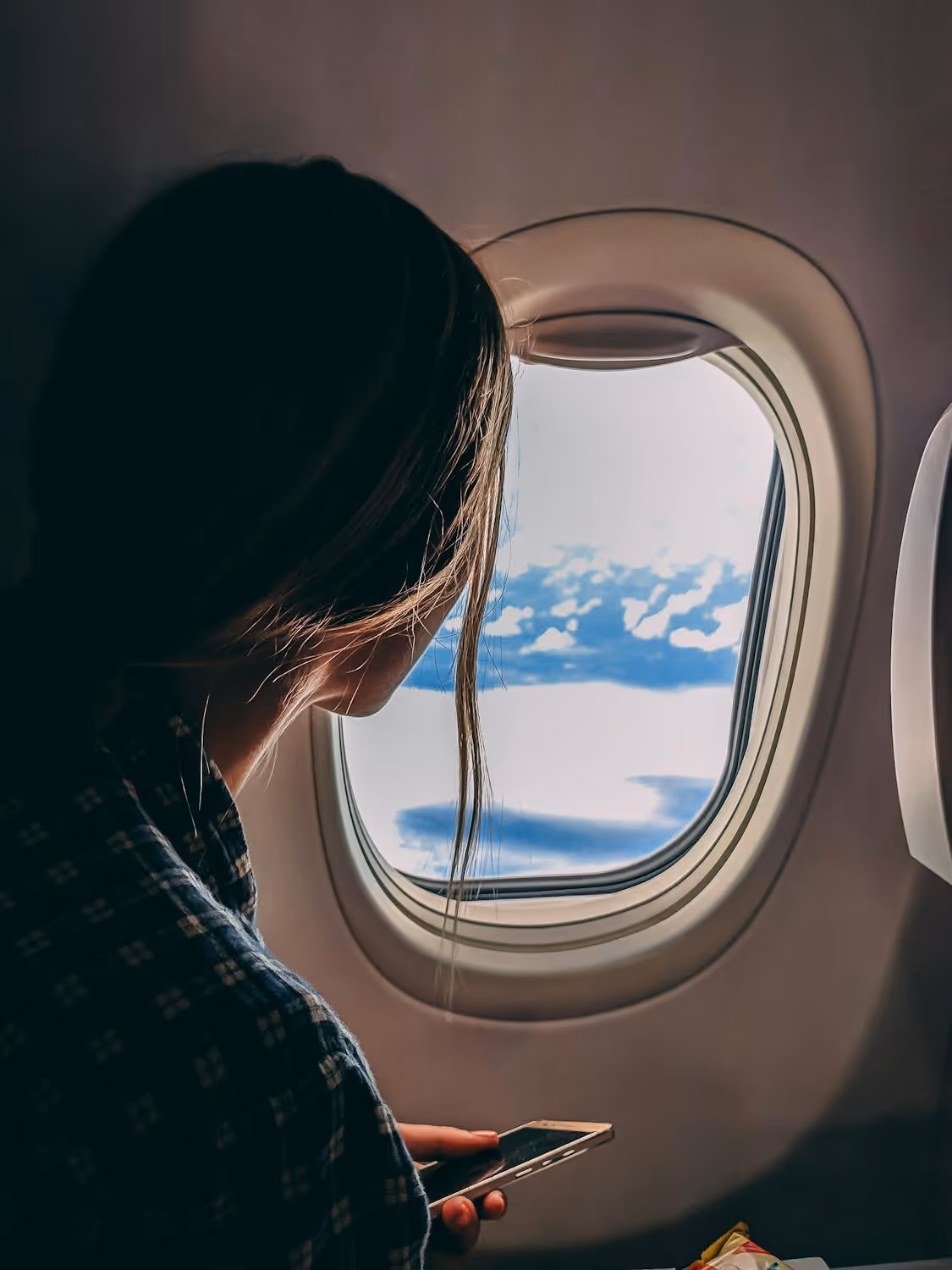 A woman on a plane holding her cell phone and looking out the window