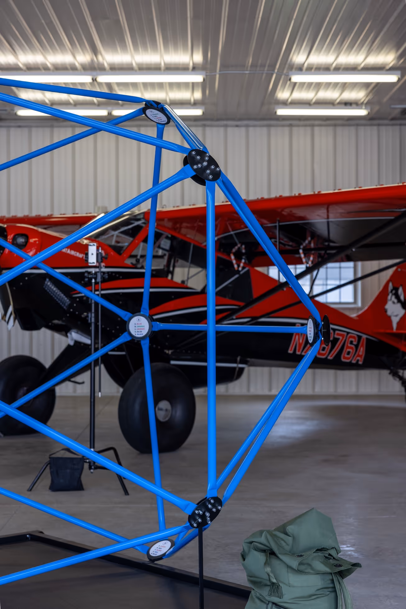 Blue geometric metal frame structure in front of a red and black small aircraft inside a hangar.