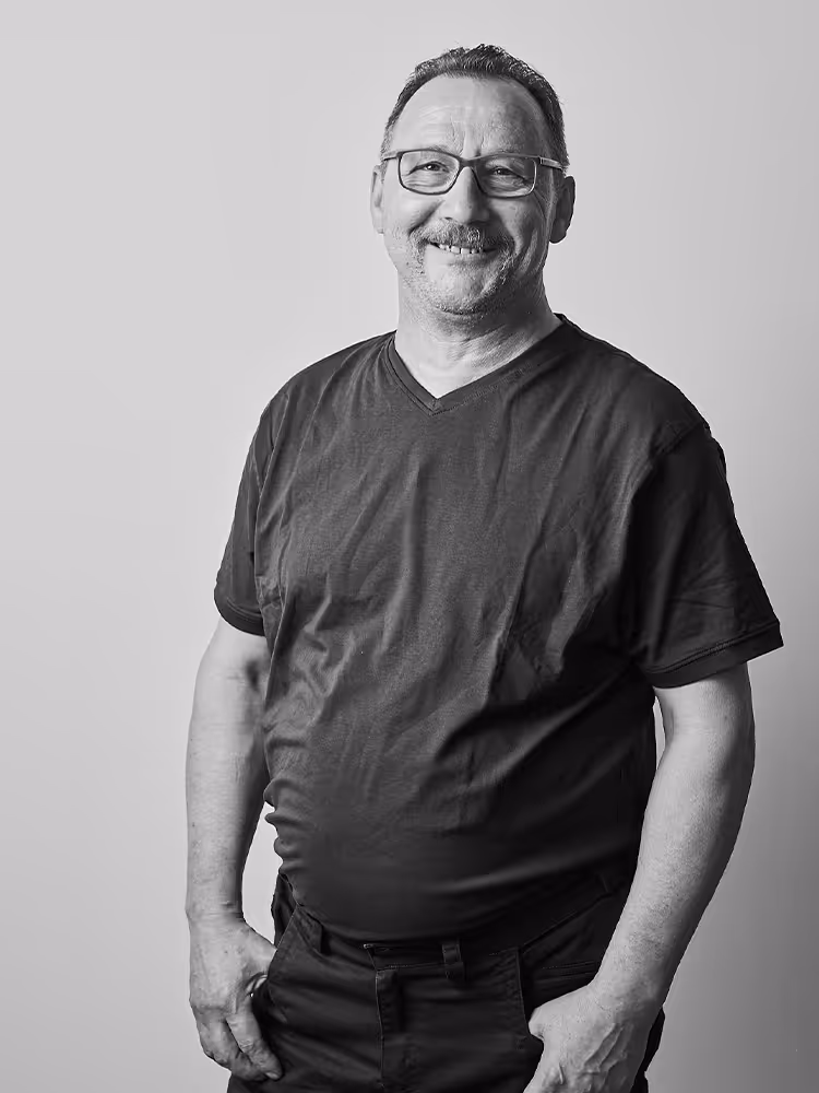 Porträt von Ivan Cernecky, Mitarbeiter bei Werndl Immobilienmanagement, freundlich lächelnd in legerem T-Shirt, mit Brille und entspanntem Auftreten vor einem schlichten Hintergrund.