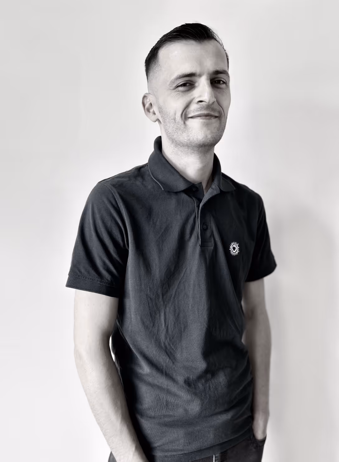 Porträt von Gentian Azemi, Mitarbeiter bei Werndl Immobilienmanagement, lächelnd in legerem T-Shirt und mit flacher Kappe, vor einem schlichten Hintergrund.