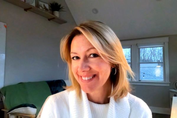 Lisa Barfield, Clear Point Designs, specializing in Local & Community Marketing, from New Providence, New Jersey, head-and-shoulders portrait of a seated woman with shoulder-length blonde hair swept to the side, smiling and wearing a white ribbed sweater and small hoop earrings, in a bright home office with two windows and a neutral wall.