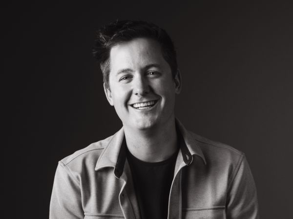 Casey Batezel, Apollo Projects, specializing in Project Management, from Fort Collins, Colorado, is pictured in a head-and-shoulders black-and-white portrait as a smiling man with short dark tousled hair wearing a light-colored collared jacket over a dark crew-neck shirt against a plain dark background.