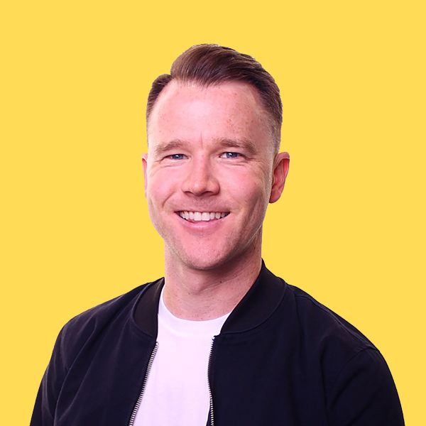 Andy Rhodenbaugh, Clear Sight Design, specializing in Squarespace, from Atlanta, Georgia, head-and-shoulders portrait of a man with short light brown hair styled to the side, blue eyes, smiling, wearing a white crew-neck shirt and a dark zip-up jacket against a solid yellow background.