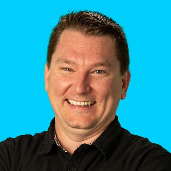 David Hepburn, Hepburn Creative, Inc., specializing in Video & Photo Storytelling, from San Diego, California, is shown in a head-and-shoulders portrait as a smiling man with short brown hair wearing a black collared shirt against a bright turquoise background.