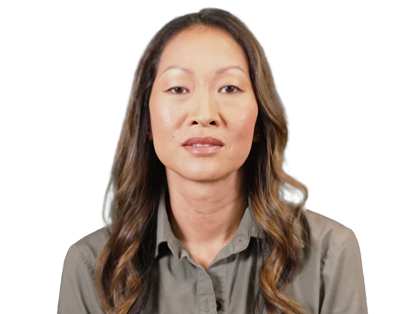 Portrait of a woman with long wavy hair wearing a gray button-up shirt against a black background.