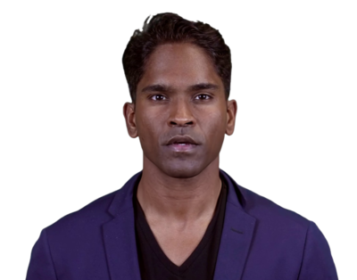 Portrait of a young man with short hair wearing a dark blue blazer and black V-neck shirt against a plain background.