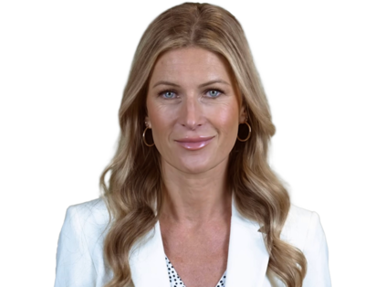 Smiling woman with long blonde wavy hair wearing a white blazer and gold hoop earrings.