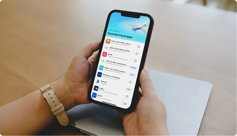 Person in a gray suit holding a credit card and using a smartphone next to an open laptop and a coffee cup on a table.