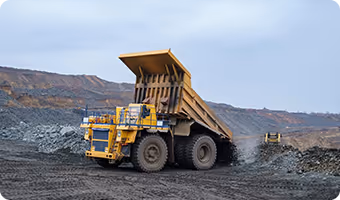 Large yellow mining dump truck unloading rocks on a mining site with hills in the background.