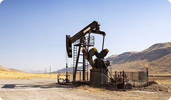 Oil pumpjack operating in a dry, mountainous landscape under clear blue sky.