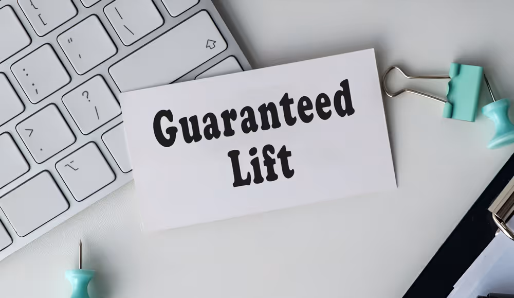 White card with the text 'Guaranteed Lift' placed on a white desk near a keyboard, binder clip, and a teal push pin.
