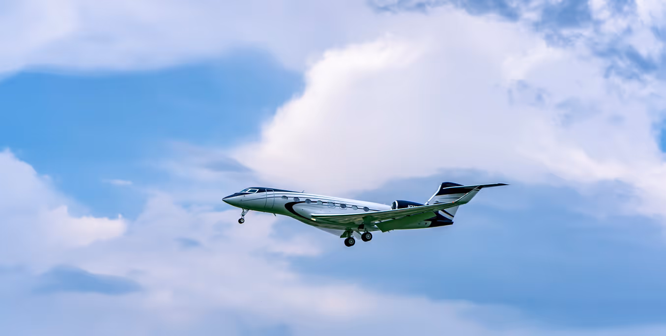 Modern private jet flying in a partly cloudy blue sky with landing gear extended.
