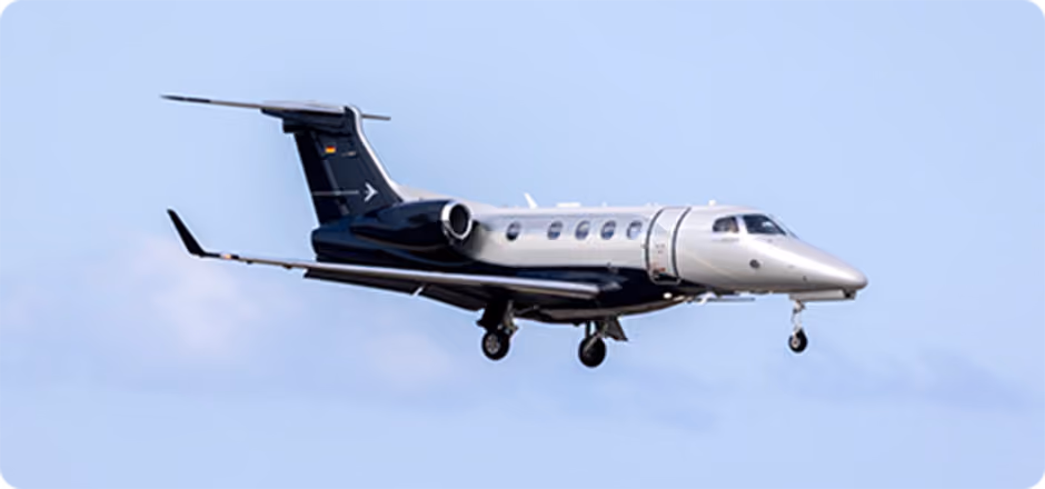 Black and silver private jet in flight against a pale blue sky.
