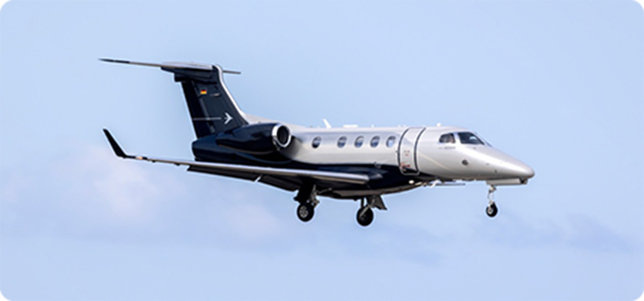 Black and silver private jet in flight against a pale blue sky.