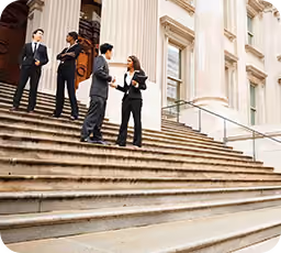Four businesspeople standing and talking on large stone steps in front of a classical building with columns.