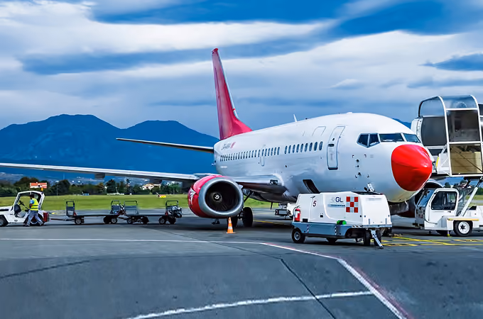 A white and red commercial airplane parked on the runway with ground crew and equipment nearby.