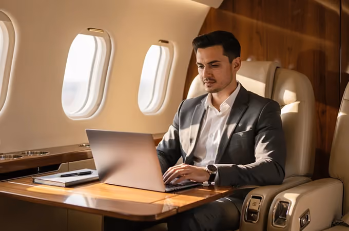 Man in suit working on a laptop inside a private jet with wooden interior and leather seats.