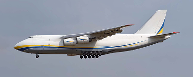 Large white cargo airplane flying against a blue-gray sky with landing gear down.