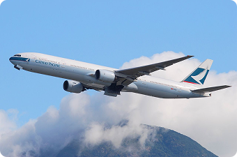 Cathay Pacific airplane flying above a mountain with clouds in a clear blue sky.