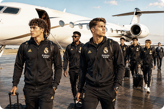 Real Madrid players walking on tarmac near a private jet wearing black tracksuits and carrying luggage.
