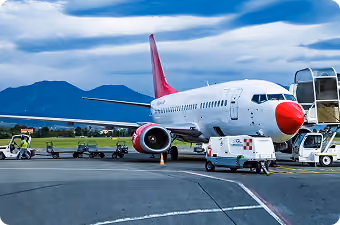 White and red airplane parked on runway with mountains and cloudy sky in background.