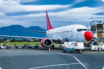 White and red airplane parked on runway with mountains and cloudy sky in background.