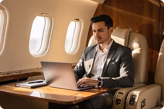Man in suit working on laptop inside a private jet with sunlight through windows.