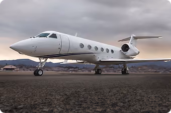 White private jet parked on runway with mountains and cloudy sky in the background.