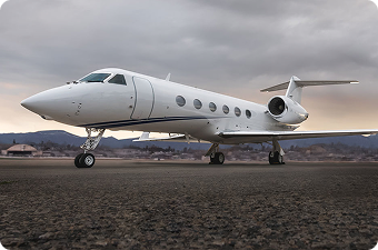White private jet parked on runway with mountains and cloudy sky in the background.