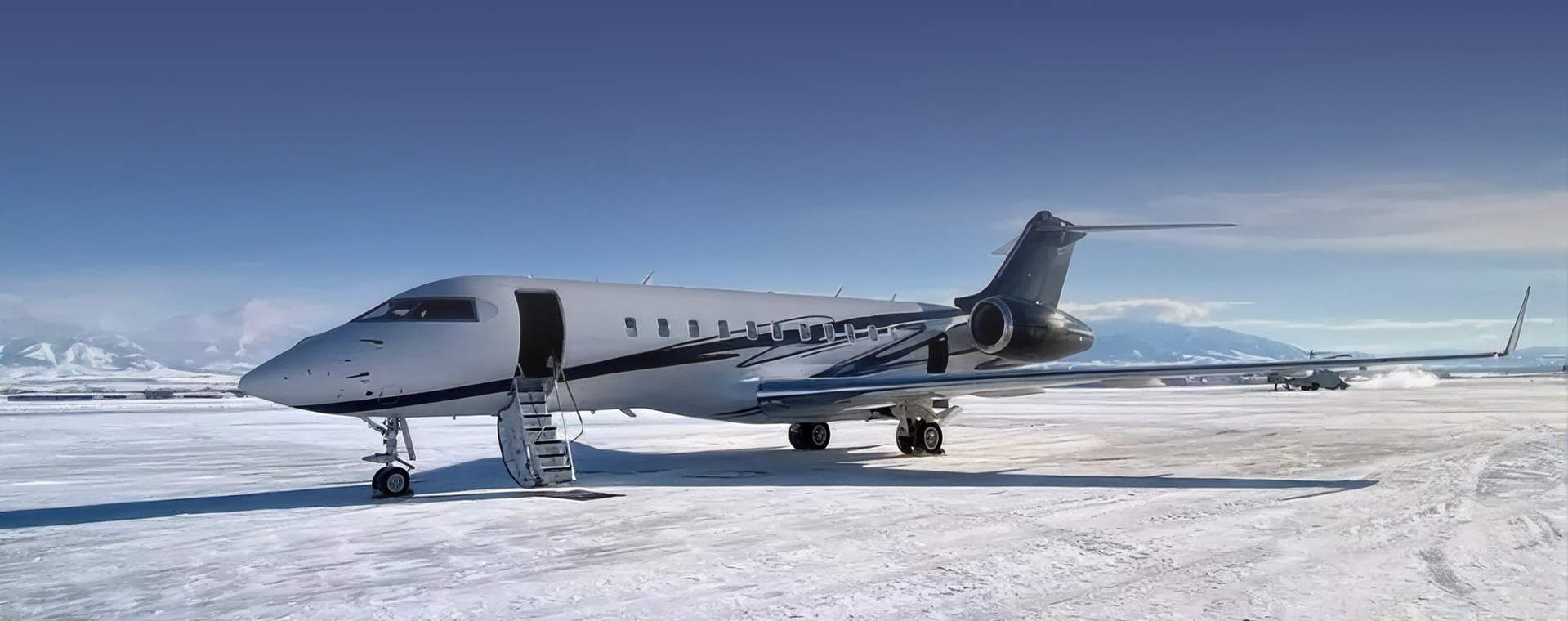 Private jet with open door and stairs on snowy tarmac under clear blue sky and mountains.