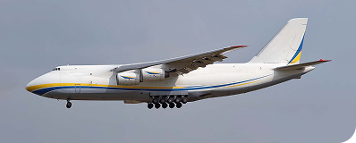 Large cargo airplane in flight with extended landing gear against a gray sky.