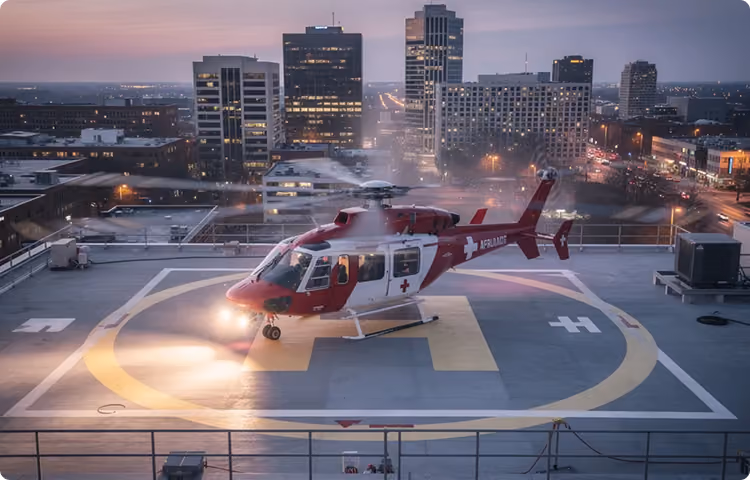 Red and white medical rescue helicopter on a downtown rooftop helipad at dusk.