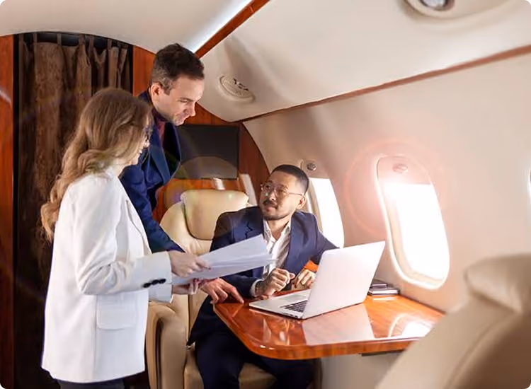 Three professionals reviewing documents and laptop on a wooden table inside a private jet.
