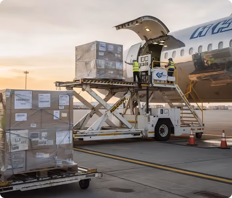 Workers unloading cargo pallets from an airplane at an airport during sunset.