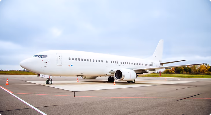 White commercial airplane parked on concrete apron at airport under cloudy sky.