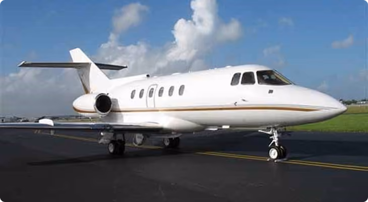 White private jet with gold stripe parked on runway under blue sky with clouds.