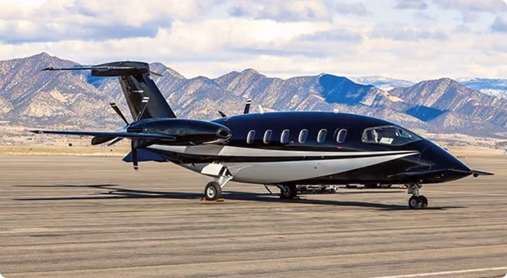 Sleek black private jet on airport runway with mountains and cloudy sky in the background.